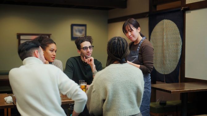 居酒屋で外国人グループからの注文を受けている女性店員