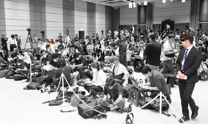 最前列右側に座る望月記者に視線を向ける運営スタッフ。手に書類を持っている。