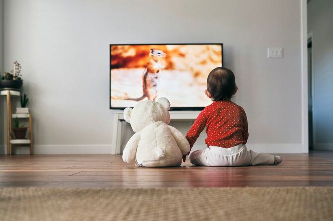 クマのぬいぐるみと一緒にテレビを見ている子供