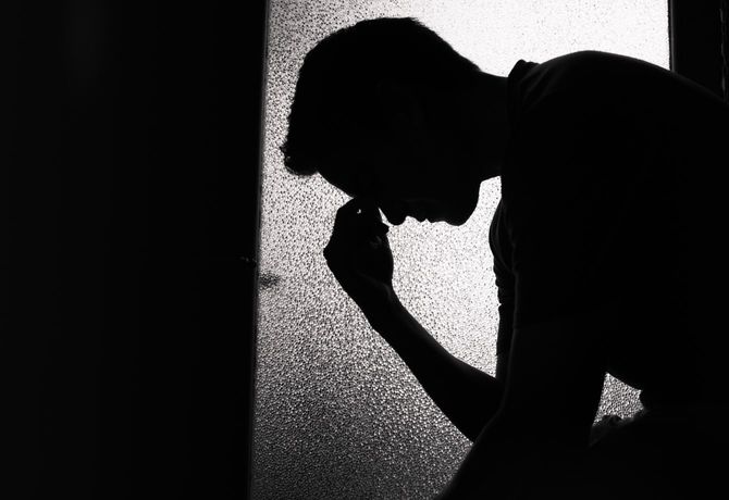 暗い部屋に座り込んでうつむく男性のシルエット