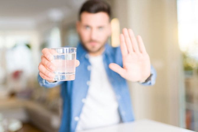 水の入ったコップを持って制止のジェスチャーをする人