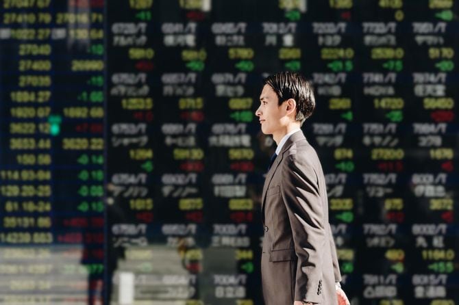 リアルタイム株価の電光掲示板の前を通り過ぎる男性