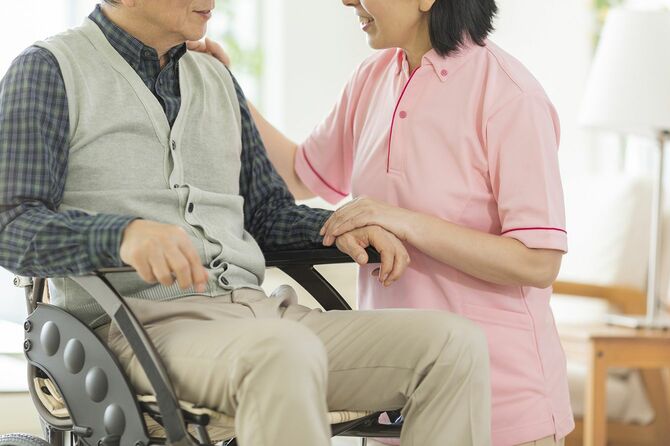 車いすのシニア男性と話す介助者