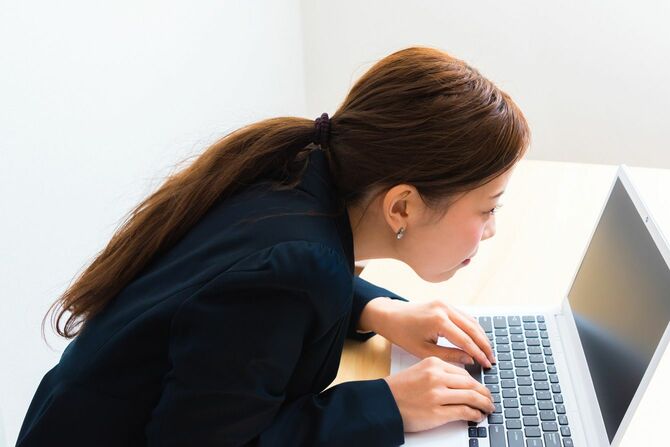 机に座りながらノートパソコンを食い入るように見つめる女性