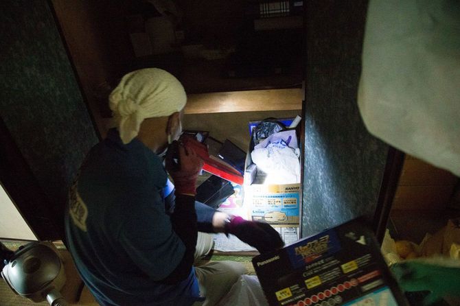 押し入れの遺品を懐中電灯で照らす作業員