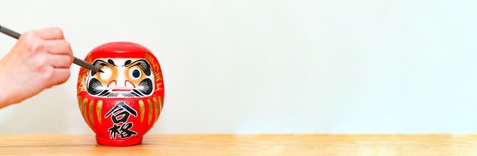 「合格」と書かれただるまに目を入れる人の手