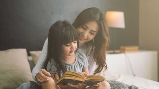 寝室で娘に本を読み聞かせる母親