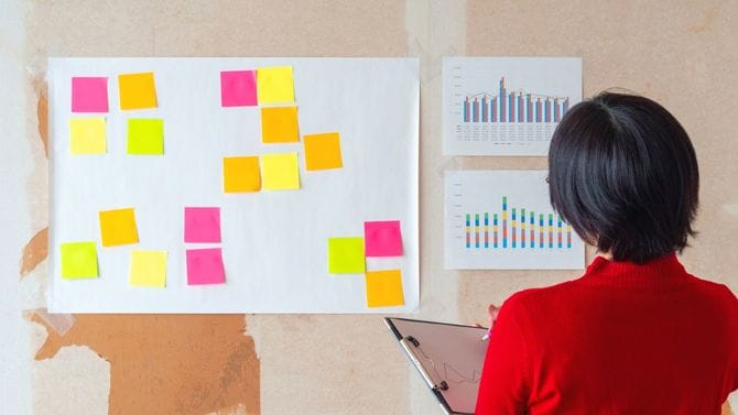 課題と数字データを壁に貼って考える女性