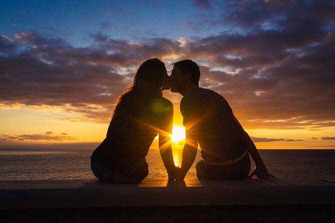 海に沈む夕日を背にキスをするカップル