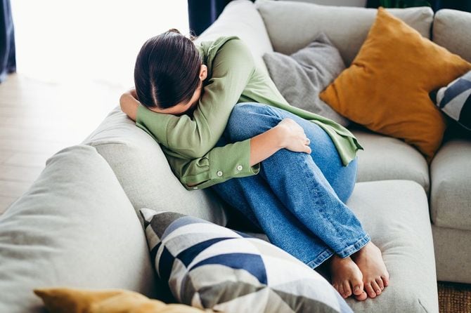 ソファに膝を抱えて座り、顔をうずめる女性