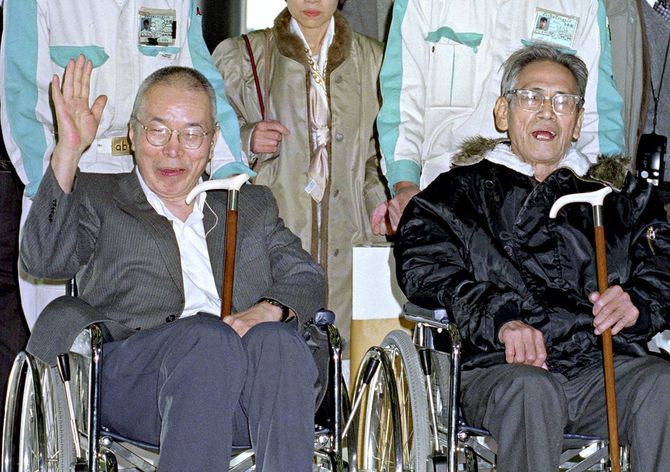 45年ぶりに帰国、手を挙げて出迎えの人たちに応える橋本恵之さん(左)とホッとした表情の田中清明さん。2人はタイ、マレーシア国境のマラヤ共産党の反英独立闘争に身を投じ、熱帯のジャングルでゲリラ活動を続けていた=1990年1月13日、成田空港