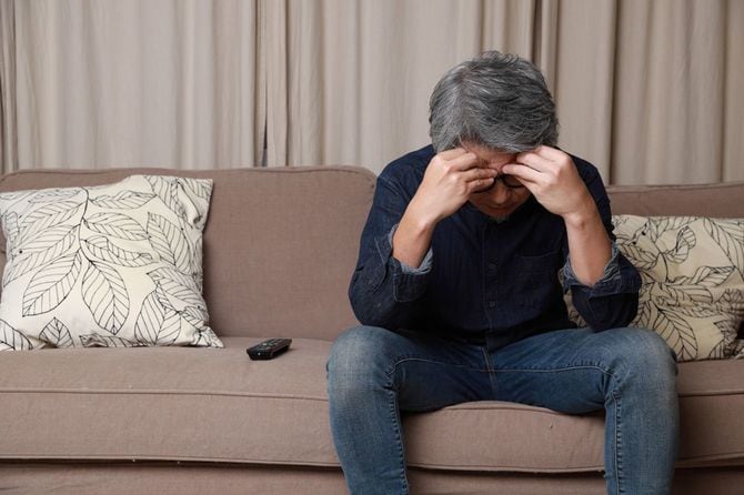 ソファに座って落ち込むシニア男性