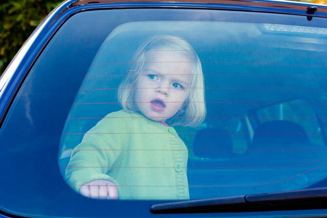 車のリアウィンドウから外を見ている、一人で社内にいる子供