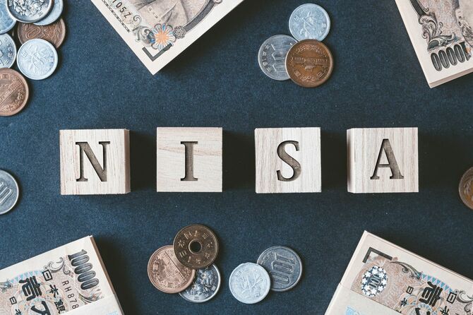 木製キューブに書かれたNISAの文字と周りに散らばった紙幣と硬貨