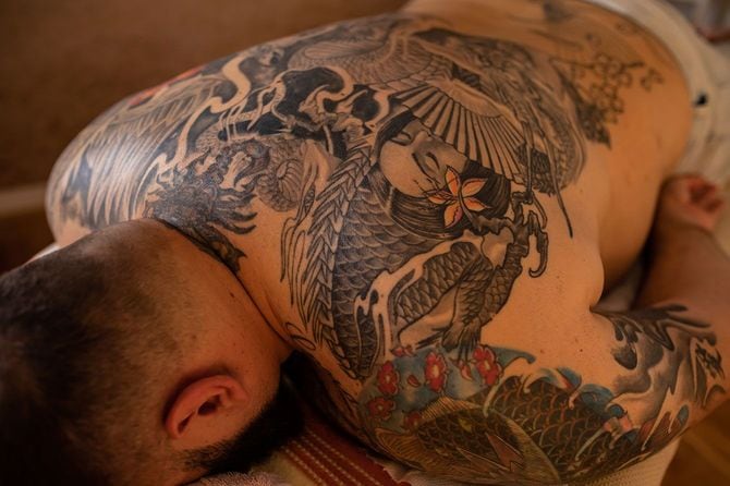 うつぶせに横たわる背中に入れ墨のある男性