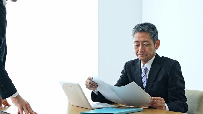 中年のアジア人ビジネスマンが部下から報告を受ける