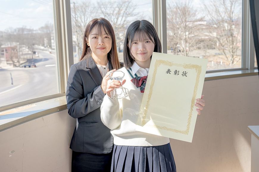 表彰状とトロフィーを持った女子高校生と教師