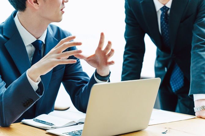 会社のデスクで同僚と話をする男性