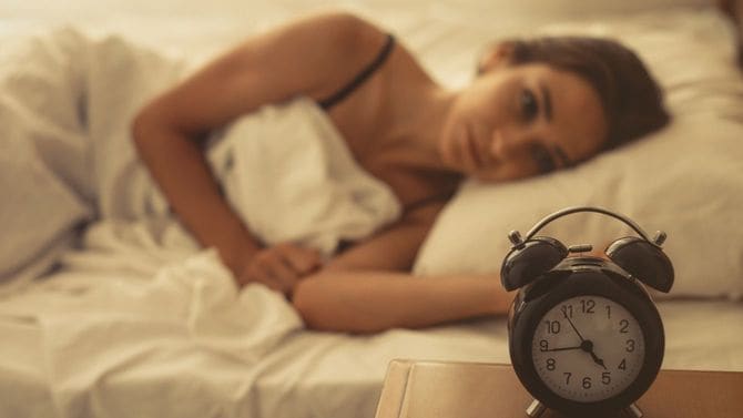 ベッドで横になる若い女性。時計は4時44分を指している。