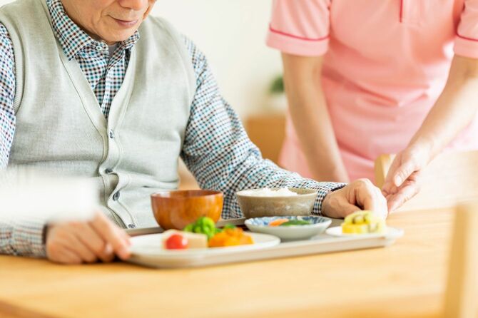 介護施設で高齢男性に食事を提供する介護士