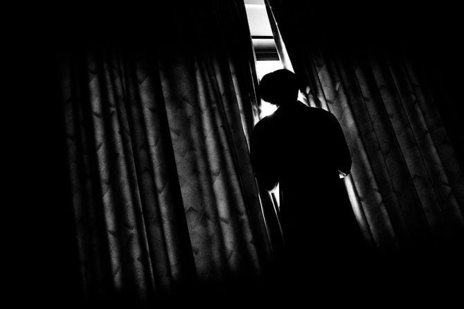 カーテンの隙間から外を見る人