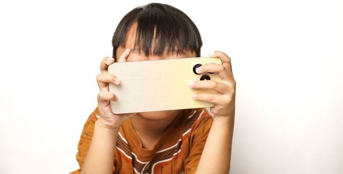 小さな手でiPhone Proモデルを顔の前で持ちながら凝視している子供