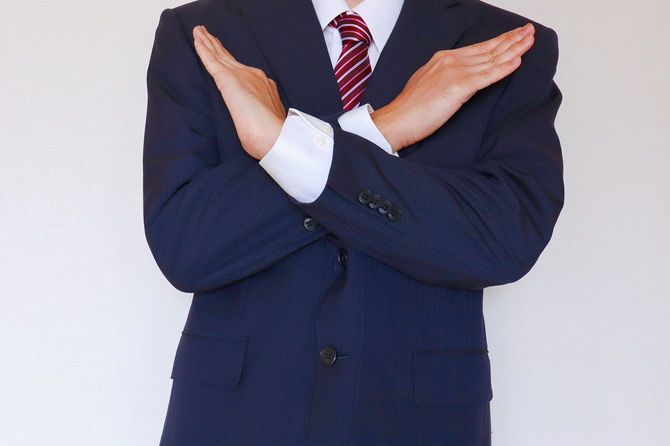 手でバツを作るスーツを着た男性