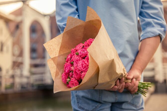 ピンクの薔薇の花束を背中に隠して、相手の到着を待っている男性