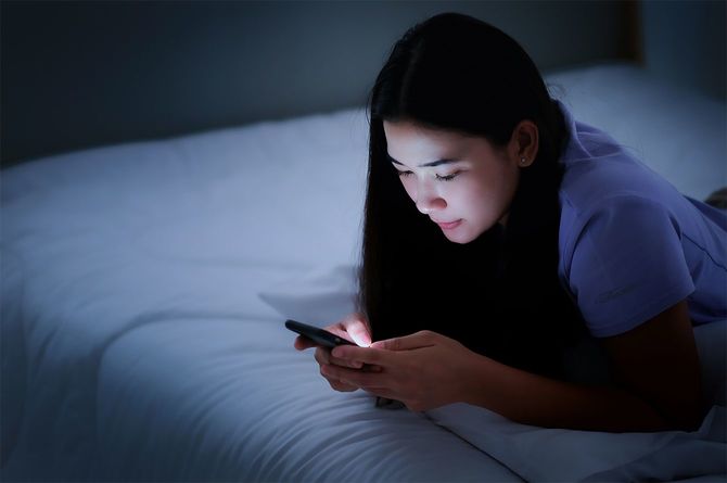 白いベッドに横たわり、夜の間にスマートフォンをプレイするアジアの若い女性