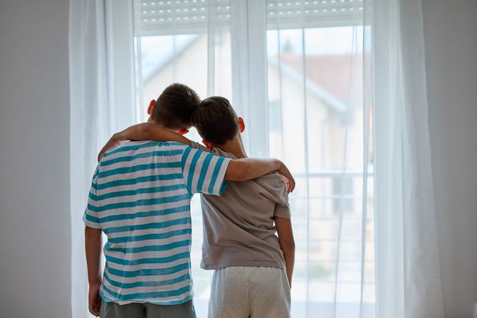 家で抱き合って窓の外を眺める二人の兄弟