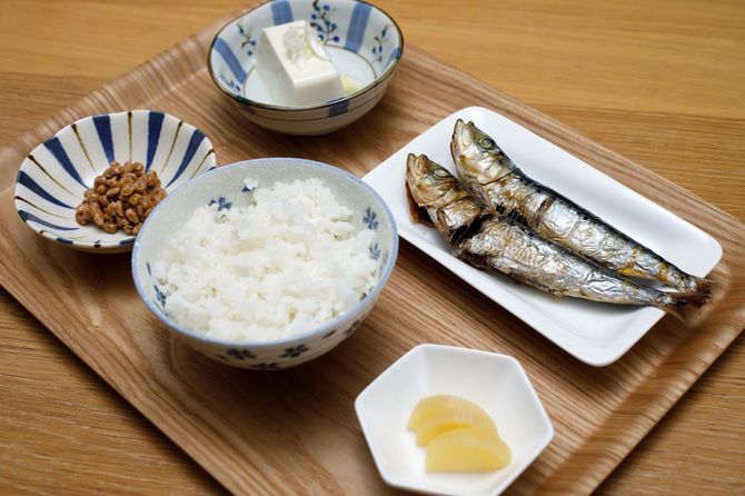 お盆の上に、ごはん、イワシ、豆腐、納豆、漬物が並ぶ