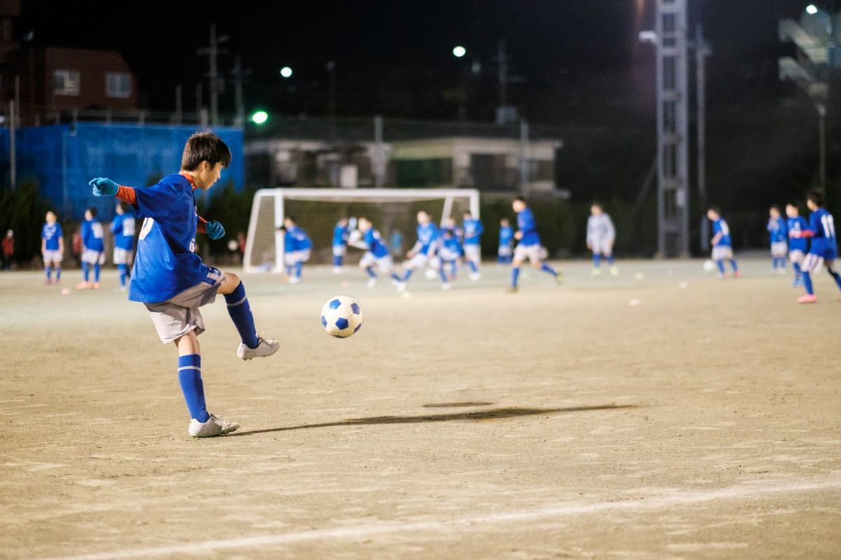 夜のグラウンドでサッカーをしている10代の日本人少年