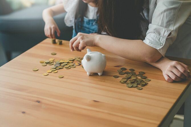 若いアジアの母と彼女の娘は貯金箱からコインを数えます。
