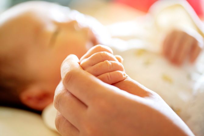 親の指を反応で握る新生児