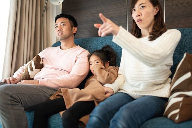 両親とテレビを見ている娘