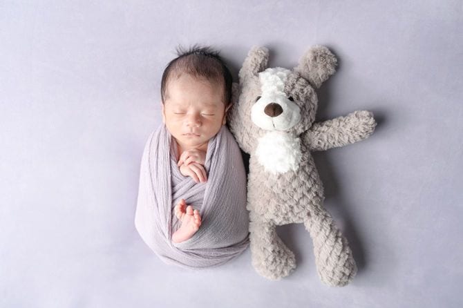 おくるみに包まれている新生児の隣にぬいぐるみ