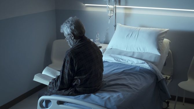 病院のベッドに腰掛け、点滴を受けながら本を読んでいる男性