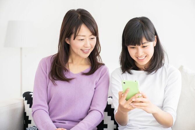 スマホを使用している娘の隣で画面をのぞき込んでいる母親