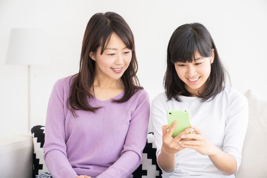 スマホを使用している娘の隣で画面をのぞき込んでいる母親