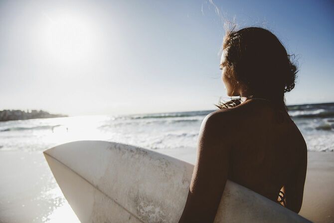 サーフボードを持ち海を見ている女性