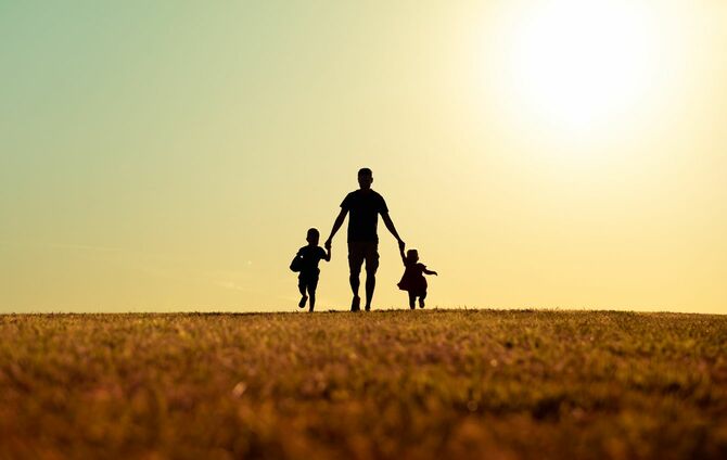 子供たちと手をつないで日没時の公園を歩く父親