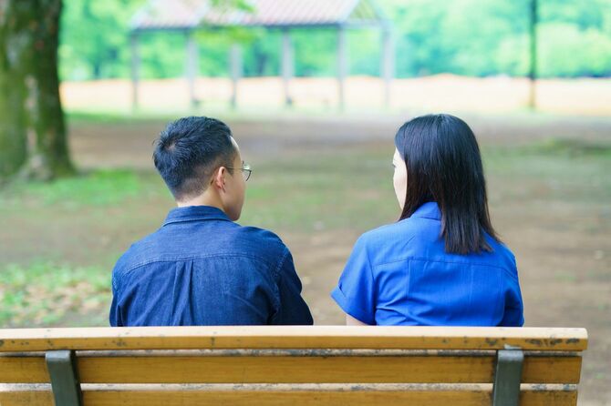 公園のベンチでおしゃべりをしている若いカップルのバックビュー