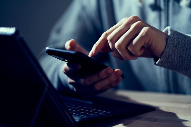 ノートパソコンを開き、スマホで入力している男性の手元