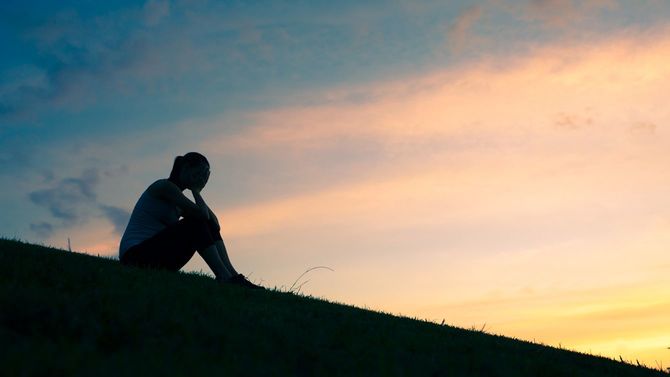 夕暮れの土手で悲しい気持ちを抱く女性