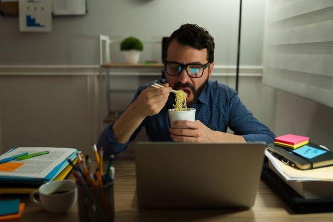 仕事をしながらカップラーメンを食べる男性