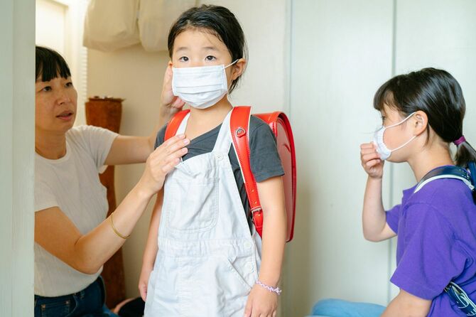 小学生の娘たちを学校に送り出す母親がマスクの位置を調整している