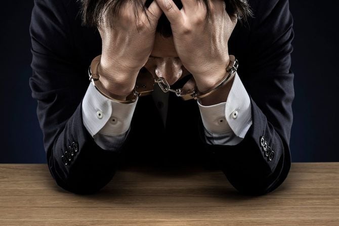 手錠をかけられ、頭を抱えている男性