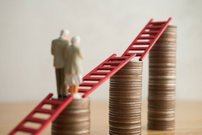 積み上げたコインの上に載せたはしごの上を歩く老夫婦の人形