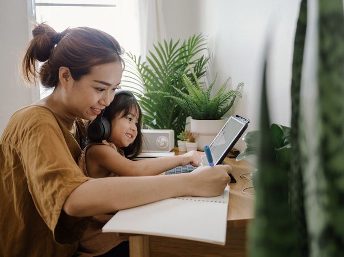 娘をひざに載せながら自宅で働く女性