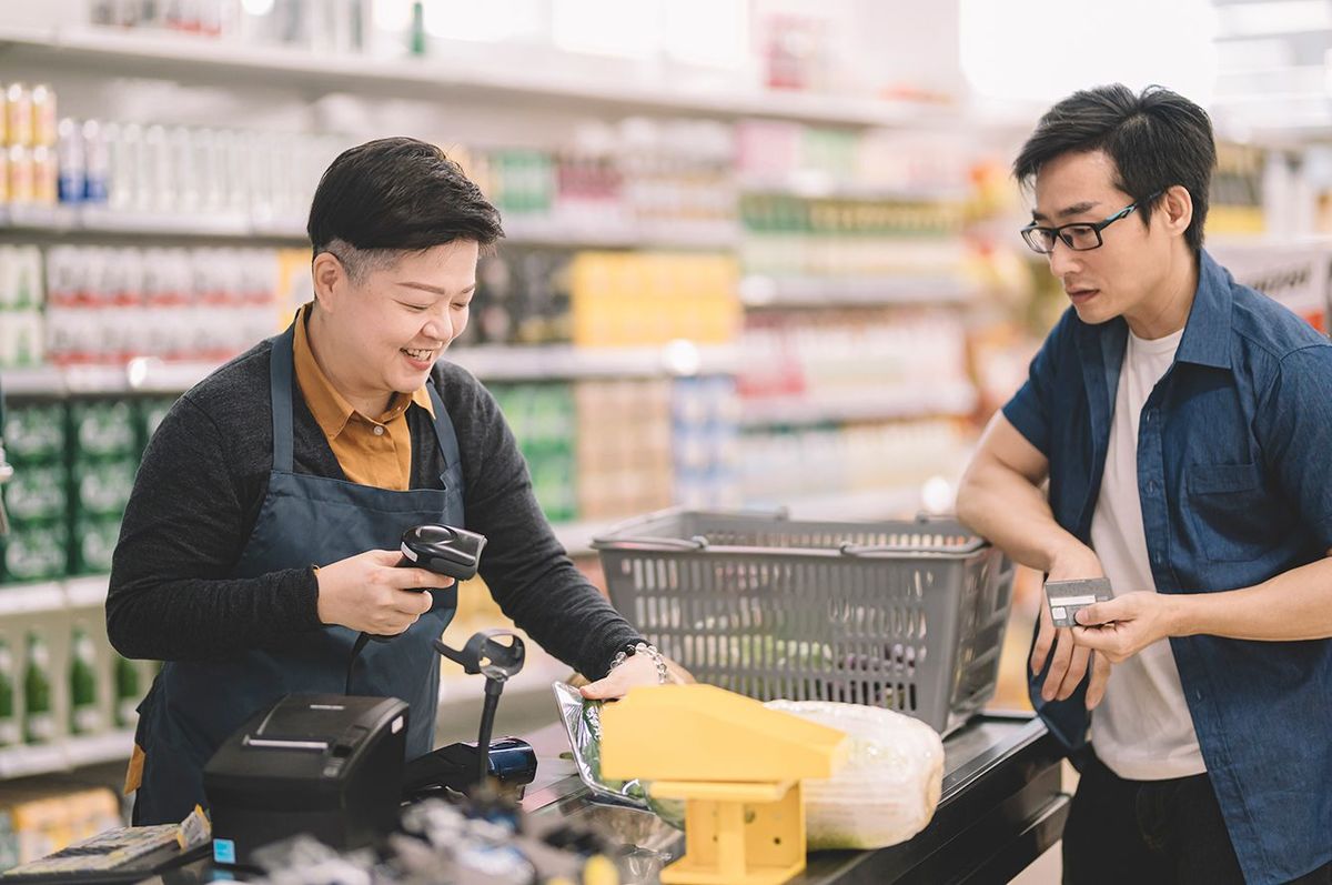 バーコードスキャナーを使用してレジカウンターでのチェックアウト時に顧客から品目をスキャンするアジアの中国の女性小売販売員レジ係